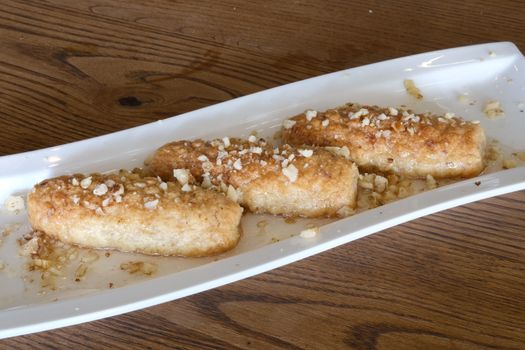 Crispy Turkish dessert rolls topped with nuts and syrup on a rectangular plate.