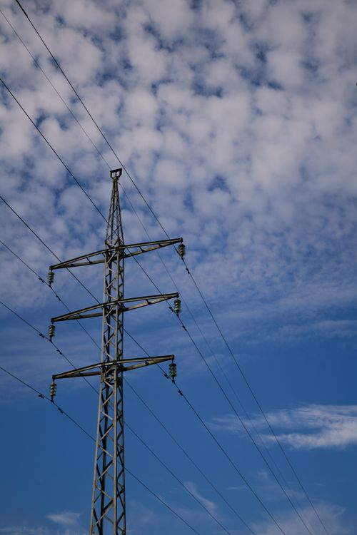 Free A high voltage power line set against a backdrop of a blue sky with clouds. Stock Photo