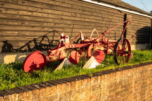 Free Rustic red plow displayed outside an old wooden barn in rural England. Stock Photo