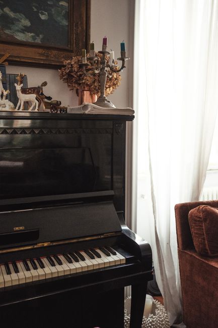 Old fashioned wooden piano with decorative elements placed near window in cozy living room with vintage interior