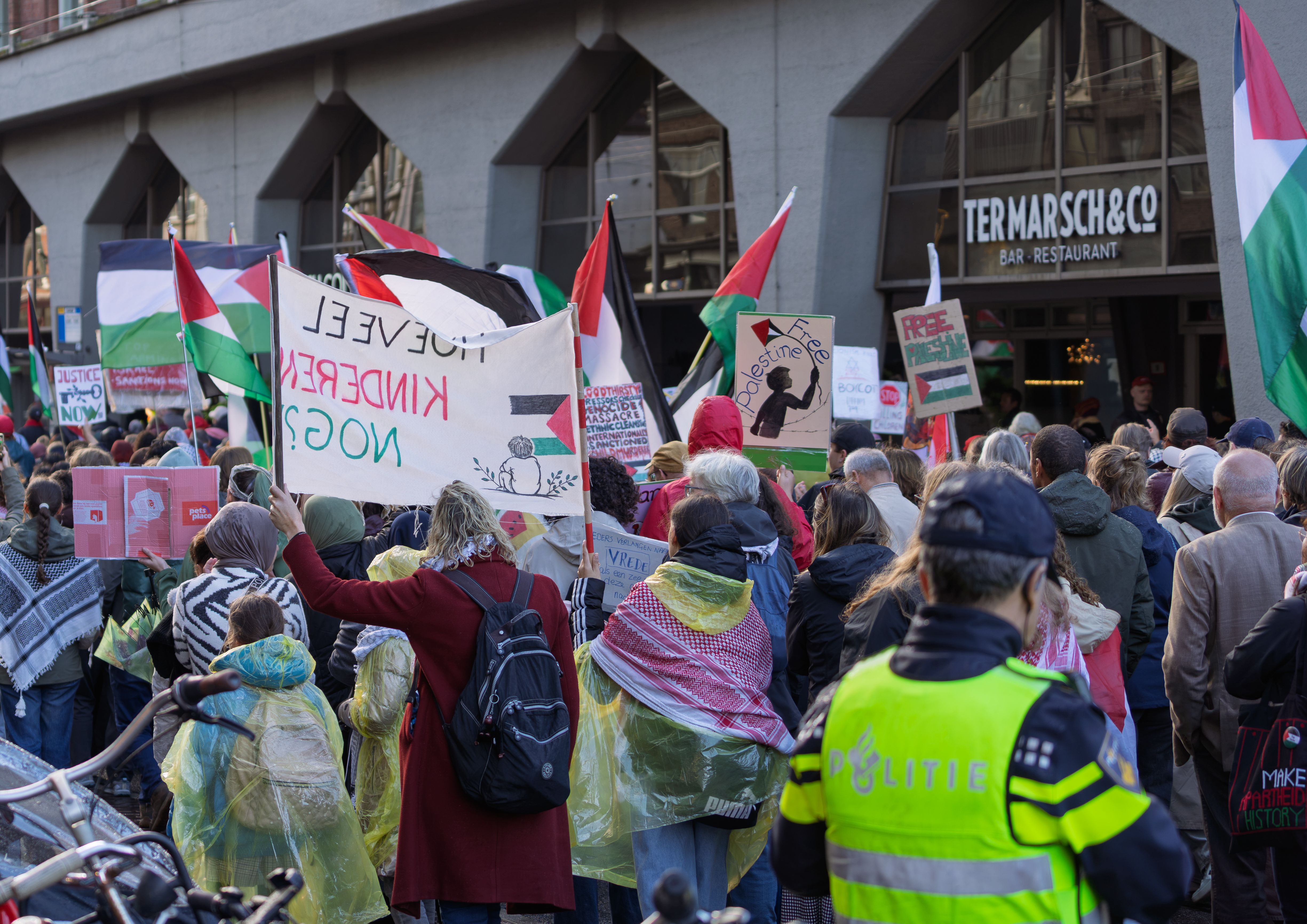 A large crowd participates in a protest supporting Palestinian rights outside a restaurant in a city.