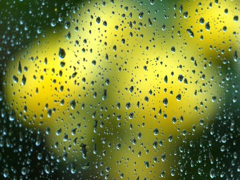 Close-up view of water droplets on glass against a vibrant yellow and green blurred background.