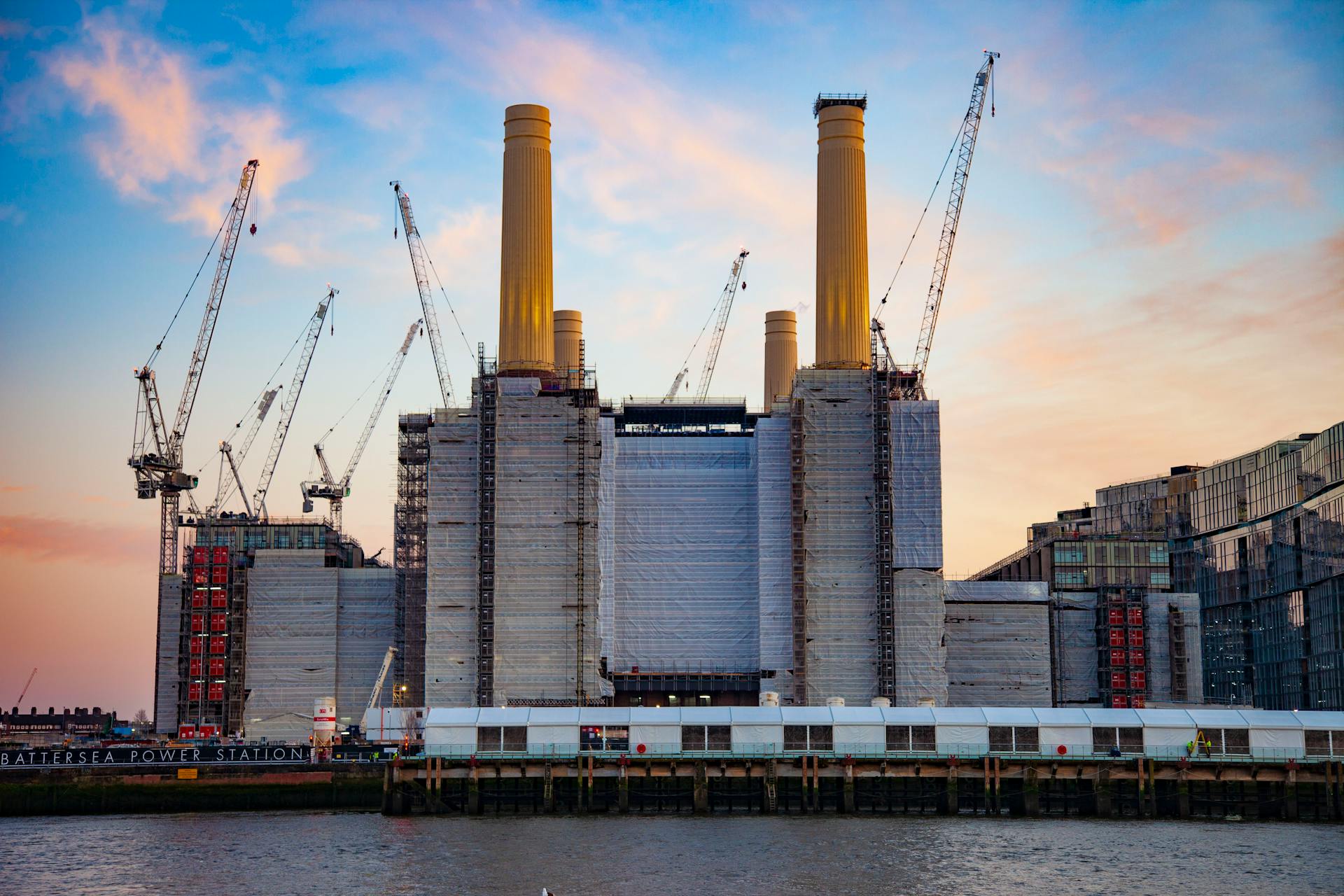 Battersea Power Station during redevelopment with cranes against a vibrant sunset sky in London, England.