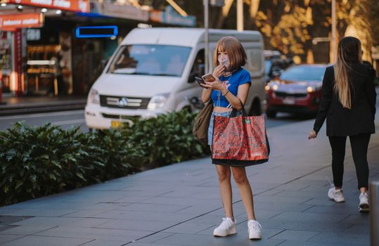 在悉尼一条繁忙的街道上，一名戴着口罩、拿着购物袋的亚洲女子