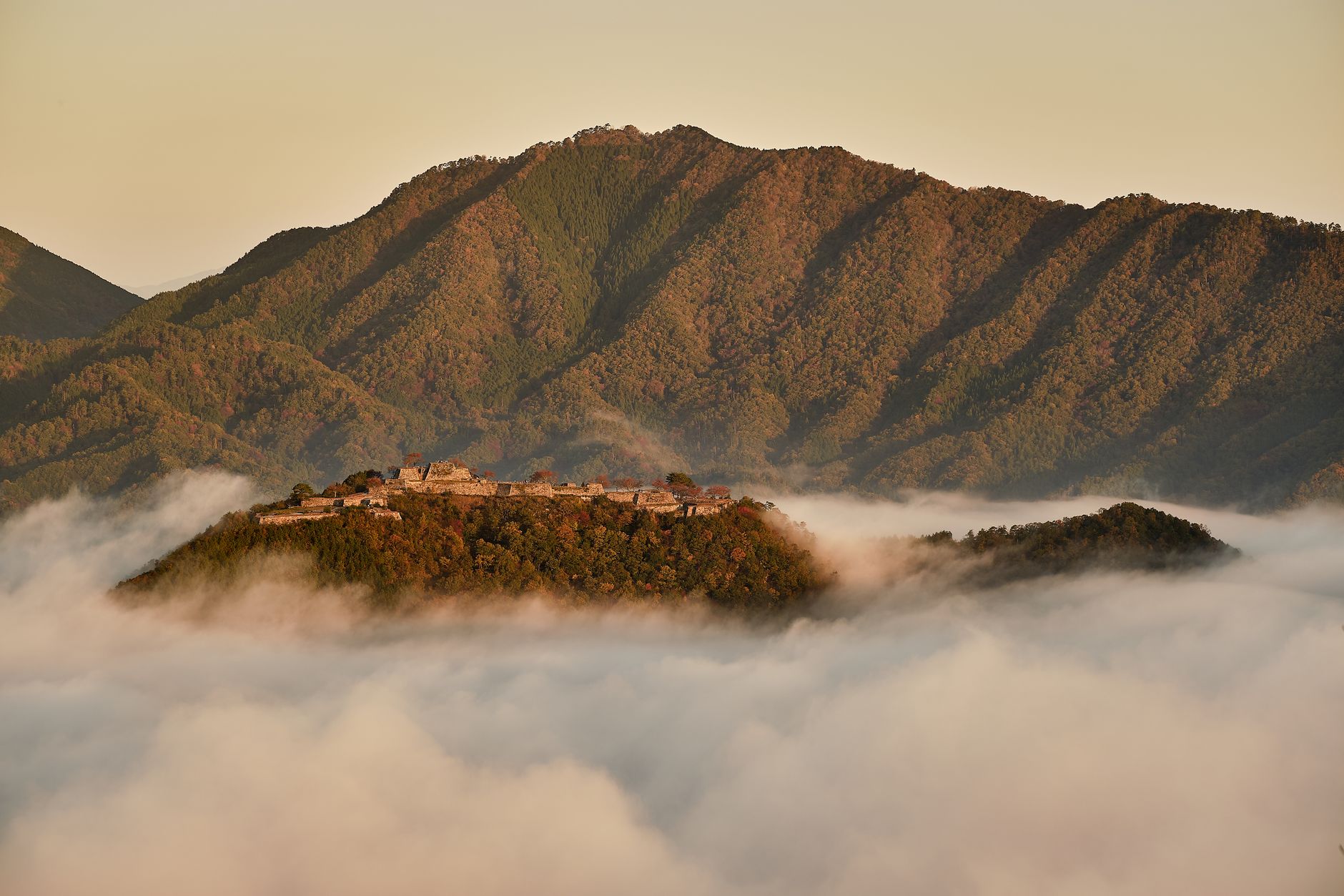 A serene view of a mist-covered castle amid lush mountains at twilight.