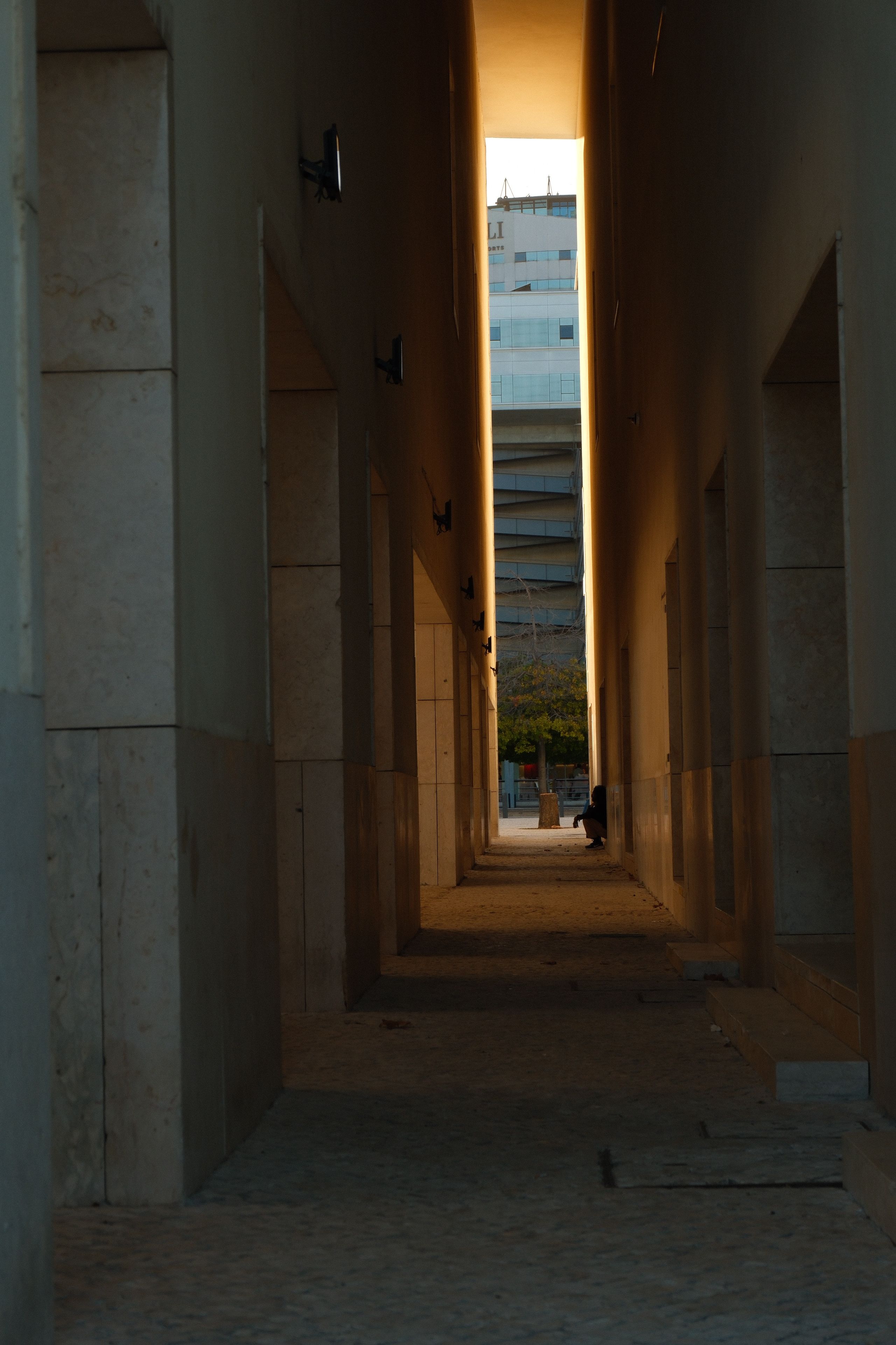 Fotomural Vista en perspectiva de un callejón urbano que conduce a un edificio, bañado por la cálida luz del atardecer.