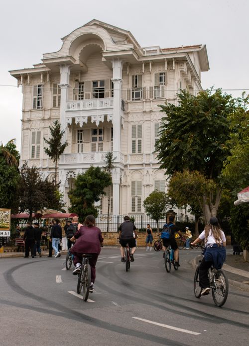 Free Group of people cycling past a grand white colonial-style building. Stock Photo