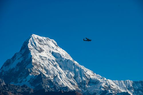 Free Small aircraft flying above a snowy Himalayan mountain peak against clear blue sky. Stock Photo