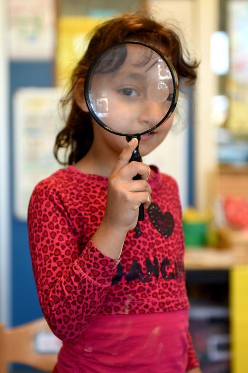 Free A young girl holds a magnifying glass indoors, showcasing curiosity and exploration. Stock Photo