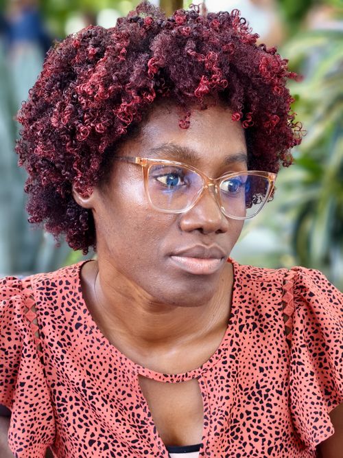 Free Stylish woman with curly red hair and glasses looking thoughtful indoors. Stock Photo