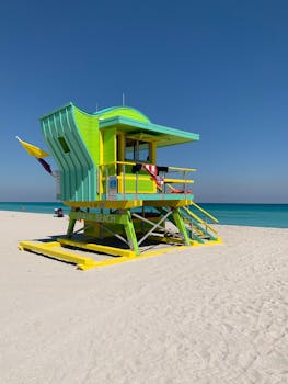 Vibrant lifeguard tower on sandy Miami Beach under clear blue sky.