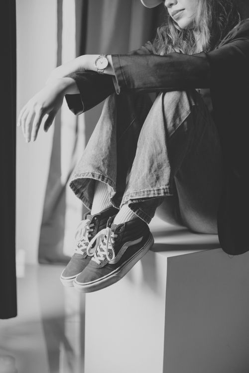 Free Stylish woman in jeans and sneakers sitting casually. Black and white tones highlight the relaxed vibe. Stock Photo
