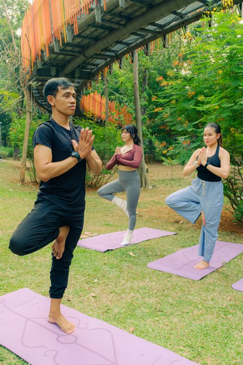 Free Three adults practicing yoga outdoors on purple mats under a metal bridge. Stock Photo