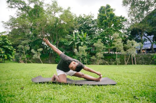 Free A man performs a yoga stretch in a serene outdoor garden setting, emphasizing fitness and nature connection. Stock Photo