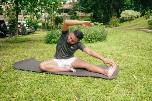 Free An adult man doing yoga on a mat in a green park, emphasizing flexibility and wellness. Stock Photo