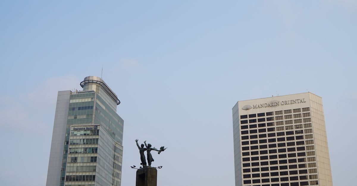 View of Mandarin Oriental and Plaza Mandiri buildings alongside a statue under a clear blue sky in Jakarta.