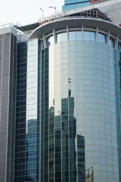 Free Urban skyscraper featuring a sleek reflective glass facade, capturing city reflections. Stock Photo