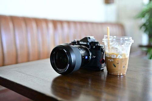 Free Close-up of a Nikon camera and iced coffee on a table in a cozy café setting. Stock Photo