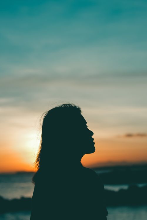 Free Silhouette of a woman gazing at the vivid horizon during sunset, creating a serene and contemplative mood. Stock Photo