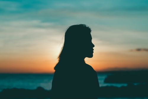 Free Silhouette of a woman against a vibrant sunset sky by the sea, evoking tranquility. Stock Photo