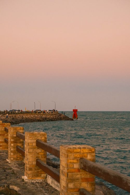 Free Serene sunset view at Ponta Negra Beach, featuring a red lighthouse and warm skies. Stock Photo