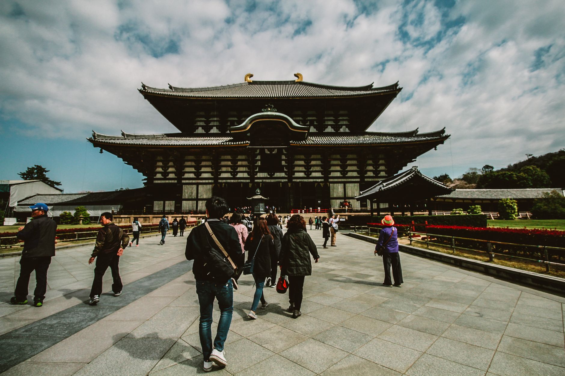 Visitors on the broad paved approach to the vast wooden Great Buddha Hall of Todai-ji in Nara under a dramatic sky