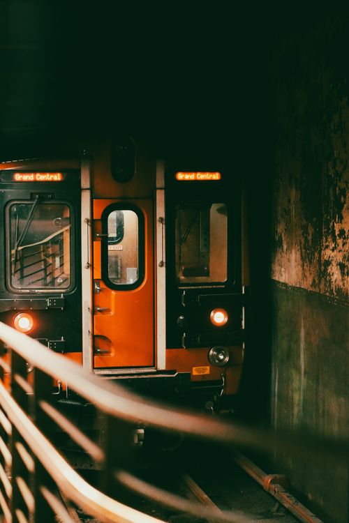 Free An orange train emerges from a dark tunnel heading towards Grand Central Station. Stock Photo