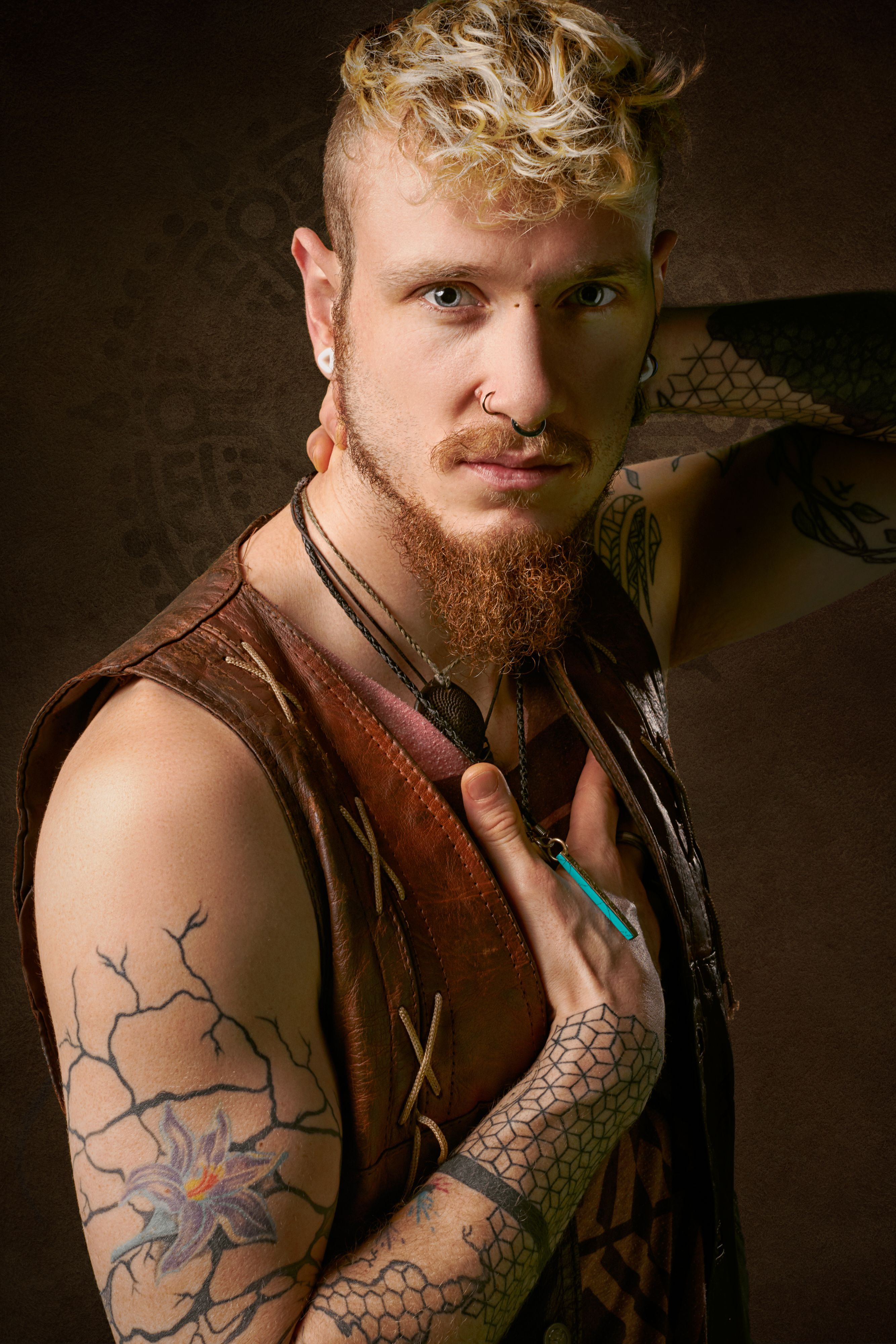 Artistic portrait of a man with tattoos and a distinctive style, featuring leather attire and piercings.