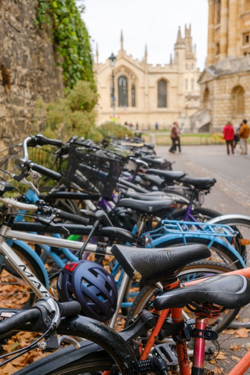 Free Row of bicycles parked on a cobblestone street next to a historic building, people walking in the background. Stock Photo