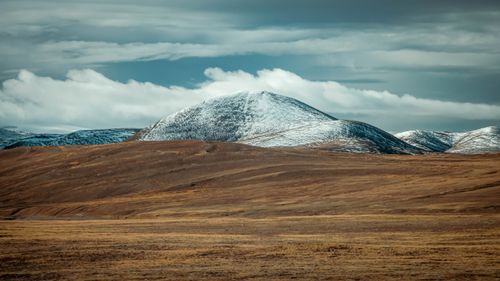 Free Serene landscape with snow-capped mountain and rolling hills under a dramatic sky. Stock Photo