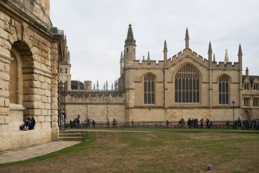 Students relax outside a historic building at Oxford University on a cloudy day.