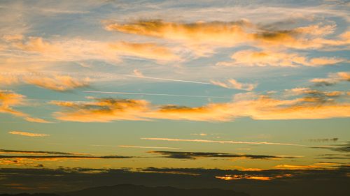 Free Vibrant sunset sky with golden clouds and distant mountains. Stock Photo