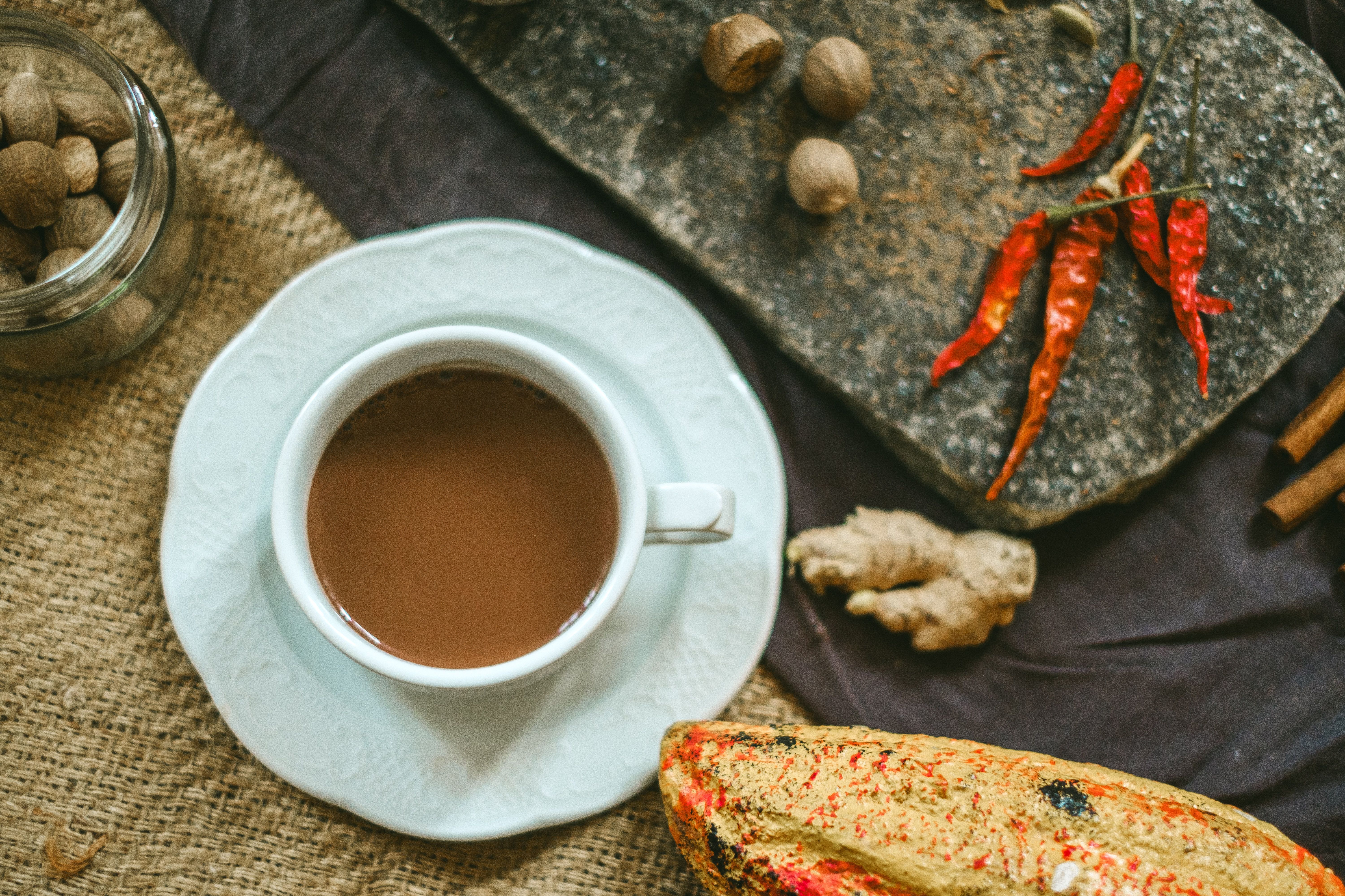 Warm cup of spiced tea with ginger, red peppers, and nutmeg on a rustic surface.