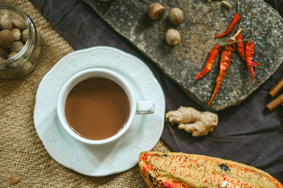 Warm cup of spiced tea with ginger, red peppers, and nutmeg on a rustic surface.