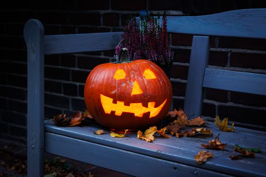 A glowing jack-o'-lantern sits on a bench surrounded by autumn leaves, creating a Halloween ambiance.