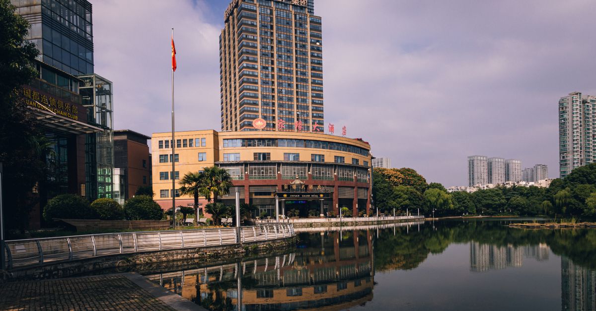 A tall modern building standing by a serene lake, surrounded by urban architecture.