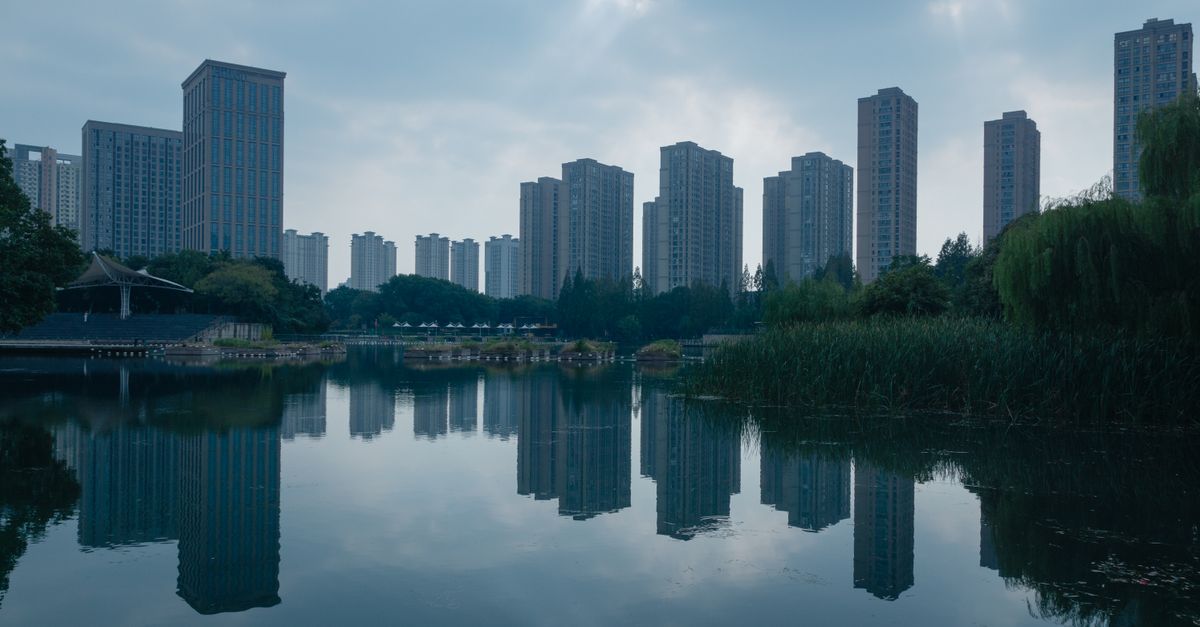 High-rise buildings reflecting on a serene lake in an urban cityscape.