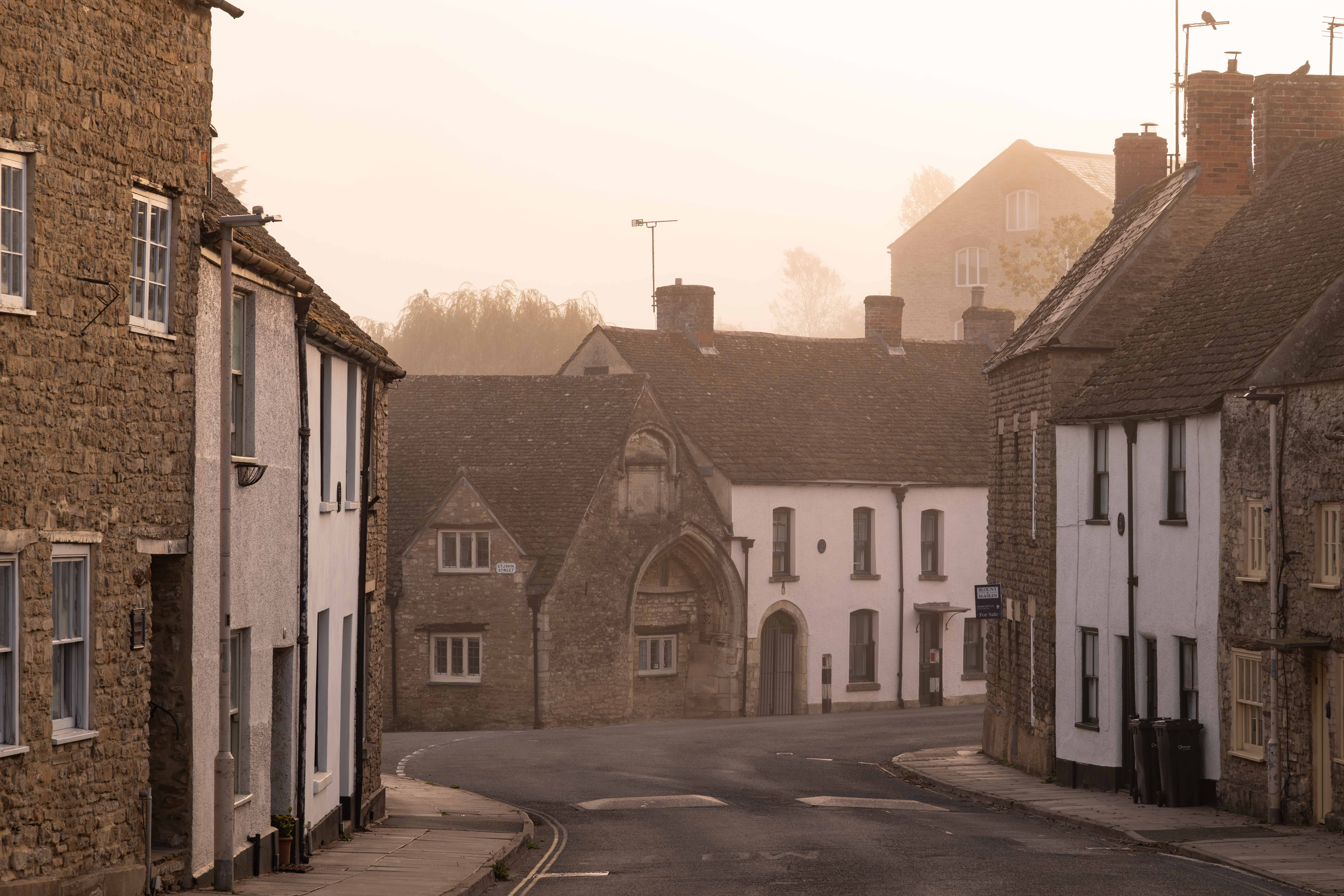 Peaceful village street with stone cottages at sunrise in a misty atmosphere.