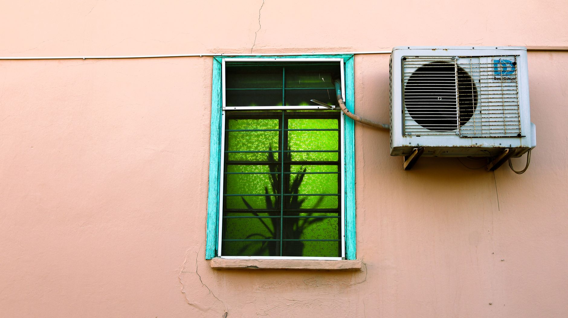 Photograph of a wall with window featuring green reflections, adjacent to an air conditioning unit.
