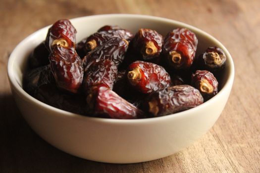 Close-up of a white bowl filled with delicious Medjool dates on a rustic wooden table.