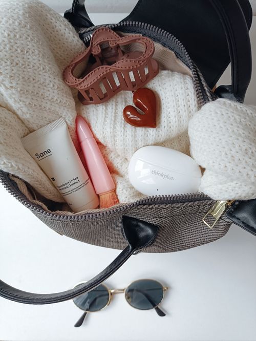 Free An overhead view of a handbag filled with fashionable accessories, makeup, and a cozy sweater. Stock Photo