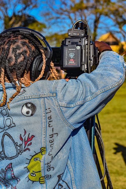 Free A young black adult filming outdoors in Malkerns, Eswatini, wearing a denim jacket with headphones. Stock Photo