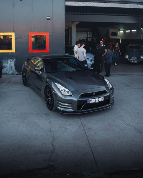 Free A sleek sports car parked outside a garage in Ankara, Türkiye, with a group of people gathered nearby. Stock Photo