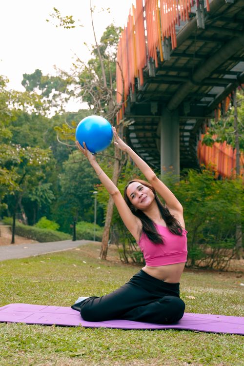 Free Woman engaging in outdoor yoga with a blue exercise ball under a bridge. Stock Photo