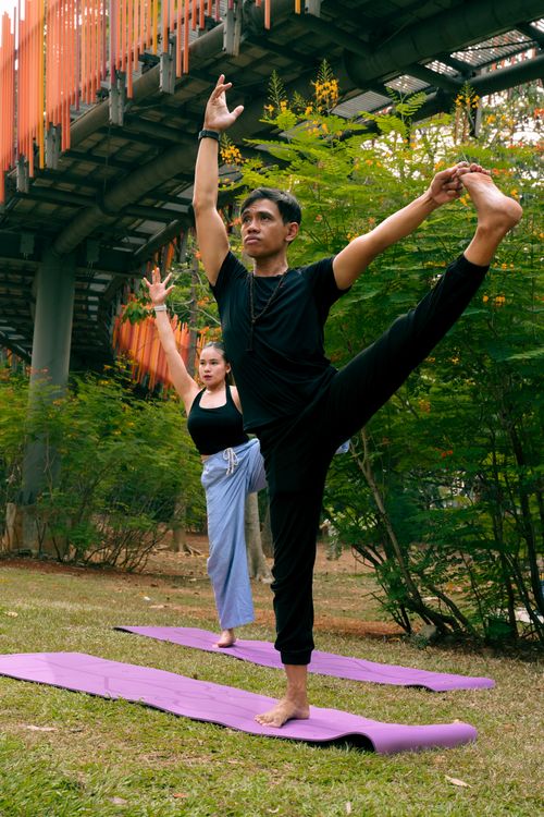 Free Two people practicing yoga outdoors under a bridge, promoting health and wellness. Stock Photo