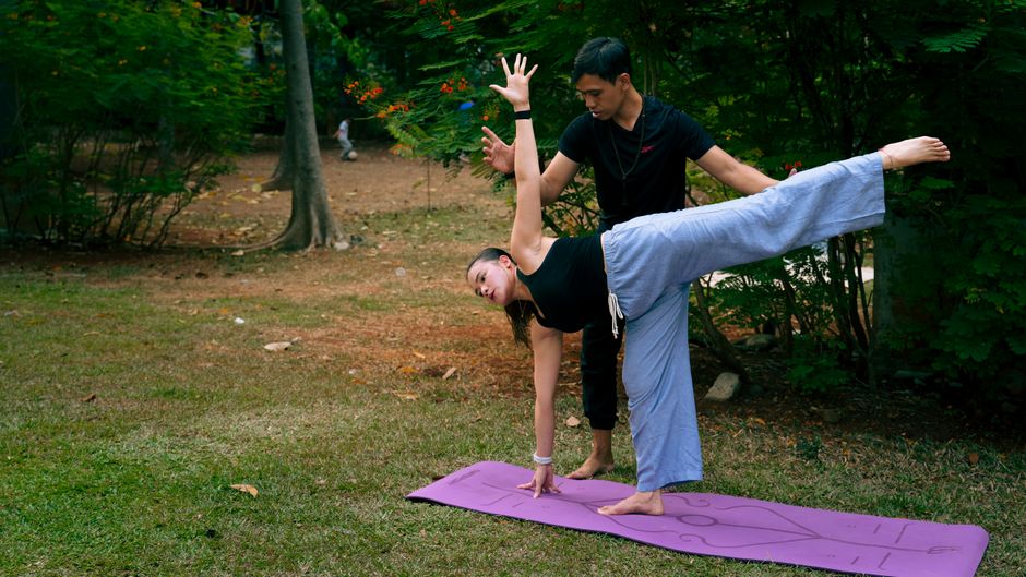 A yoga pose in a serene outdoor setting, assisted by an instructor.