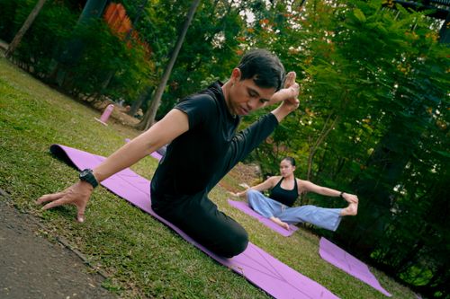 Free Two individuals practicing yoga on mats in a serene outdoor park environment. Stock Photo