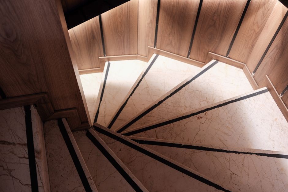 Fotomural Una escalera de caracol de diseño exquisito, con escalones de mármol y paneles de madera, que exhibe una gran elegancia arquitectónica.