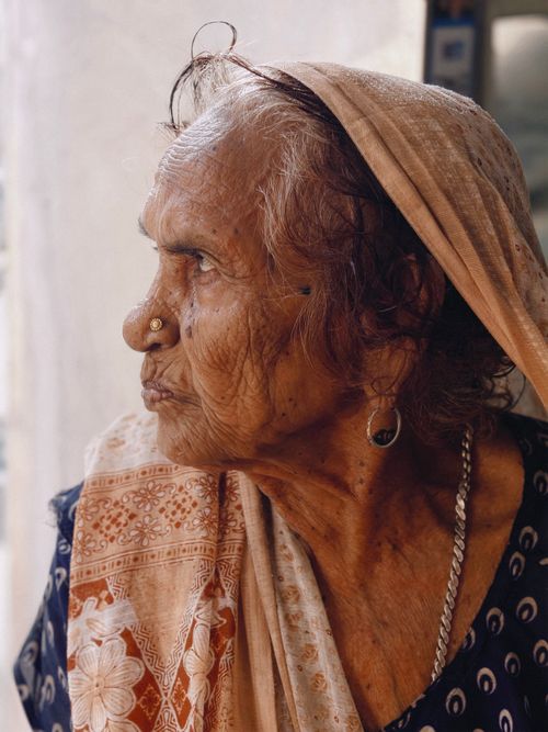 Free Portrait of an elderly woman wearing traditional attire, gazing thoughtfully to the side. Warm tones and detailed expressions. Stock Photo