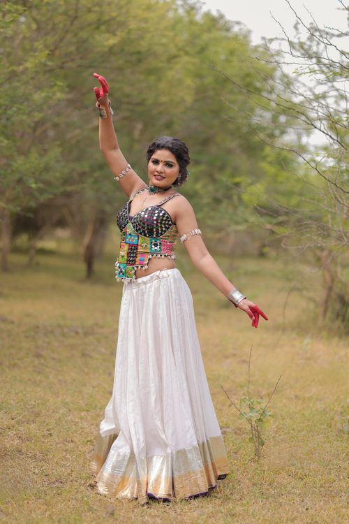 Free A woman in colorful traditional attire performs a dance outdoors, surrounded by nature. Stock Photo